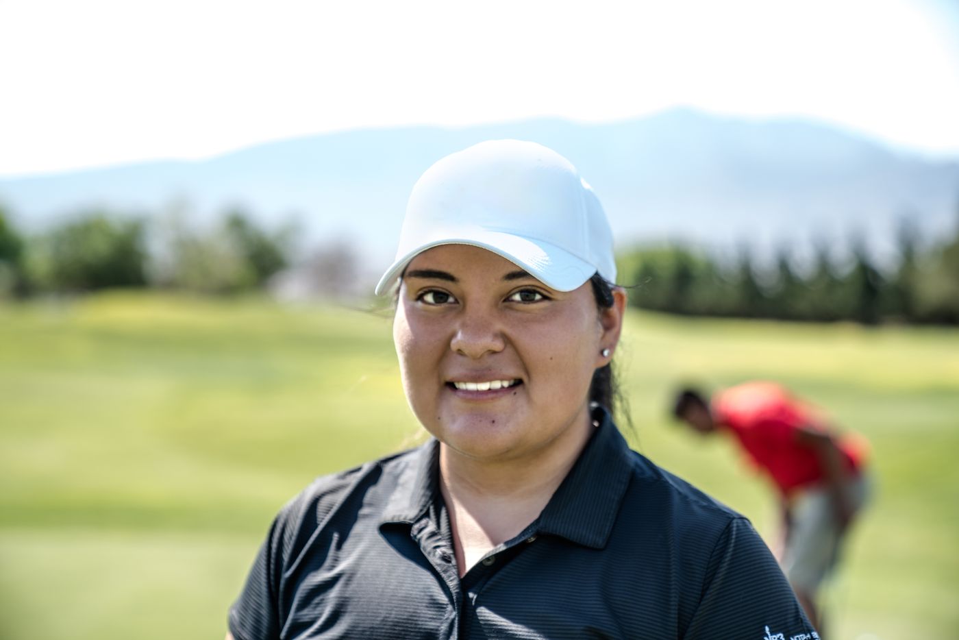 A golf coach on the practice ground, a student working behind her