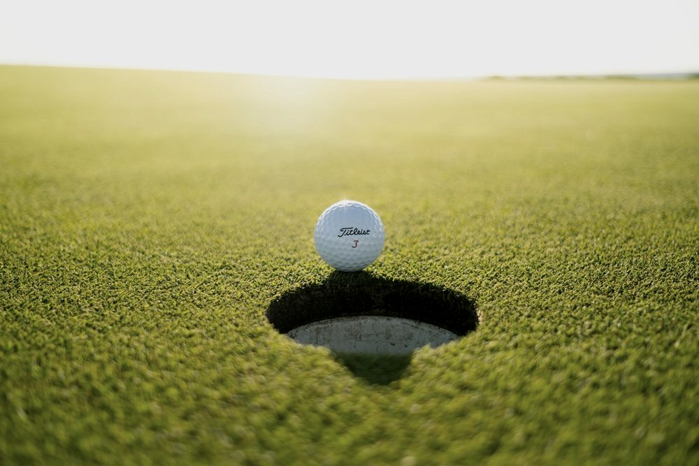 A golf ball on the lip of the hole in evening light