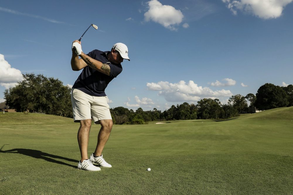 A golfer mid-swing on an open fairway under a blue sky