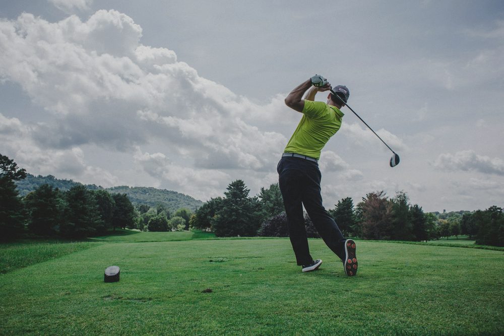 A golfer finishing a tee shot under a cloudy sky